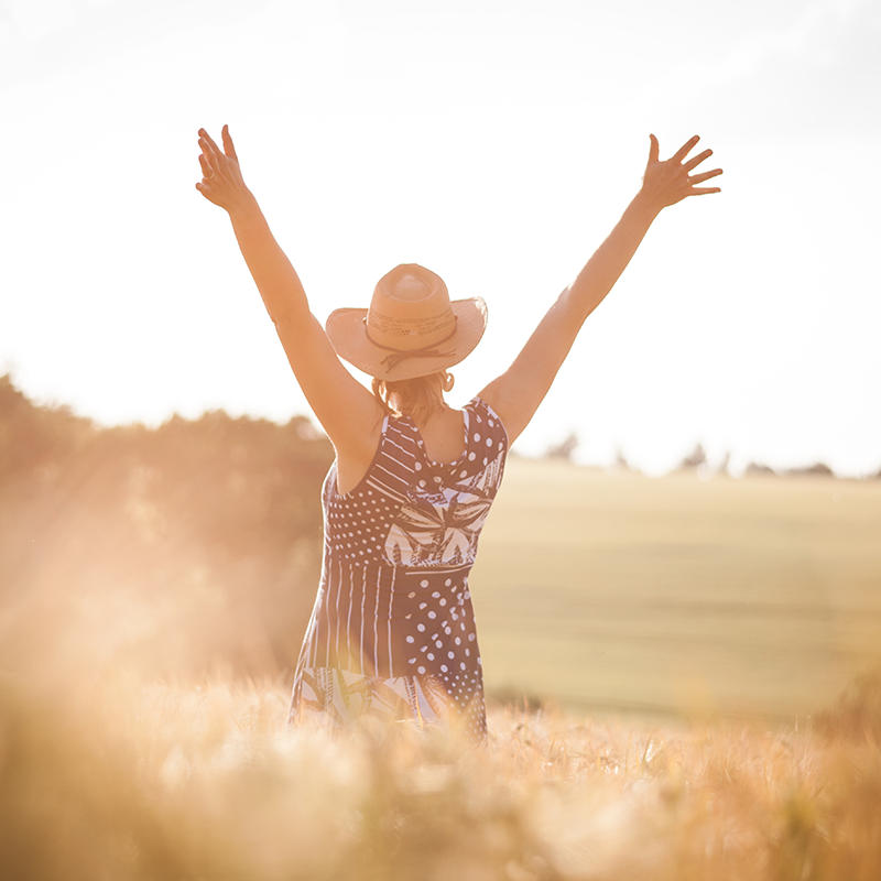 Frau im Feld mit erhobenen Händen, umarmt die Sonne.